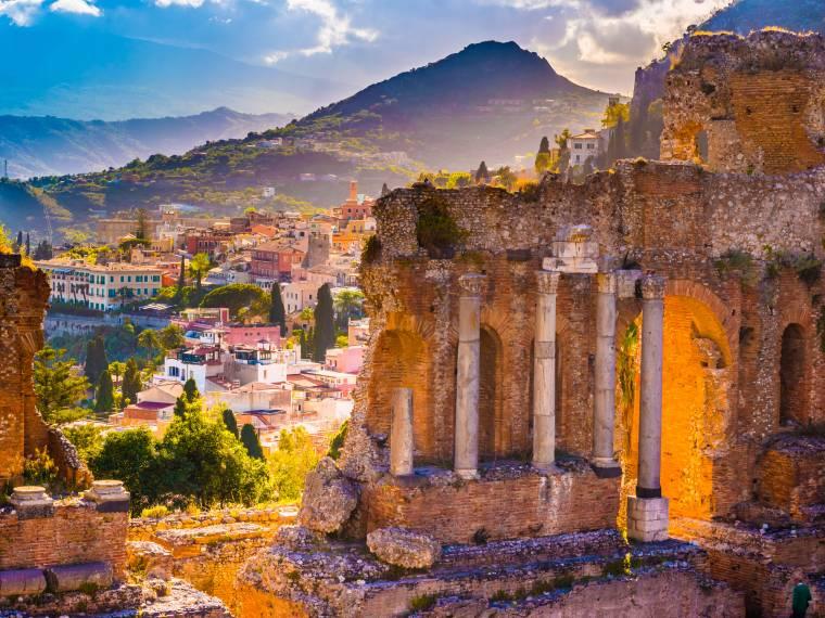 Vue sur Taormine en Sicile depuis le théâtre antique, avec les ruines au premier plan et l’Etna en arrière-plan.